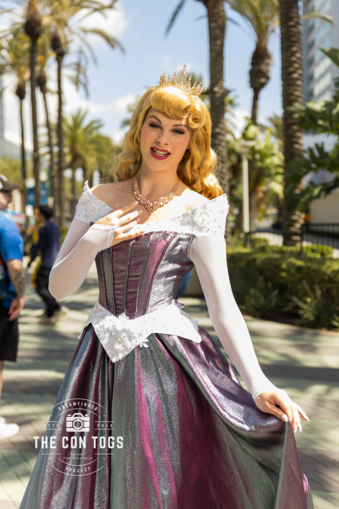 A cosplayer embodies Aurora from Disney’s Sleeping Beauty, showcasing a voluminous gown crafted from iridescent fabric that shifts between purple and green hues during Wondercon 2025.